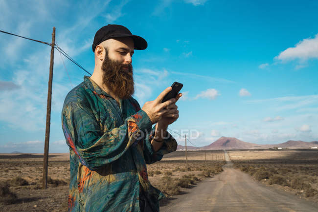 Vista lateral do homem que navega smartphone na estrada rural — Fotografia de Stock