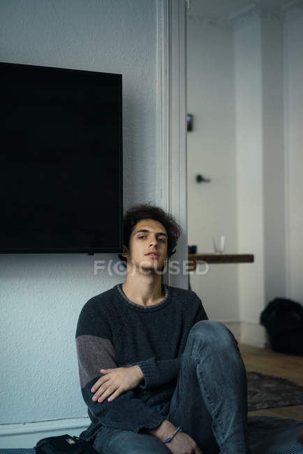 Портрет молодого человека, сидящего на полу и опирающегося на стену дома — стоковое фото