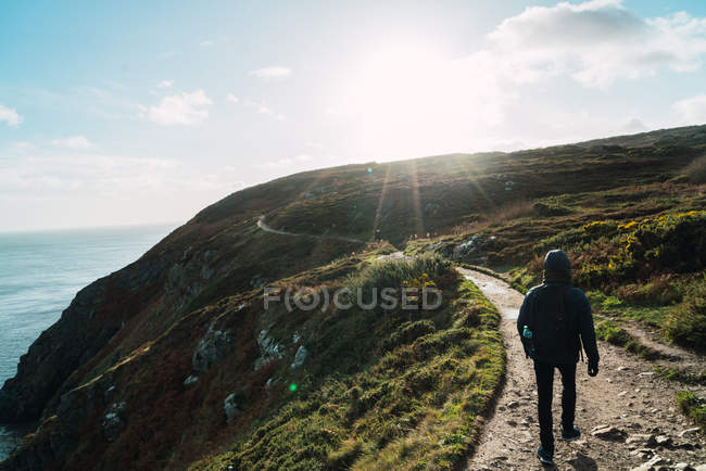 Visão traseira do turista andando na colina à beira-mar no dia ensolarado — Fotografia de Stock