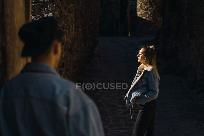 Rear view of man looking at young woman standing sensually with eyes closed in sunlight. — Stock Photo