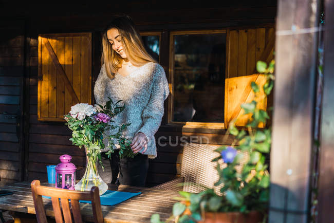 Retrato de chica rubia ajustando ramo de flores en la mesa en el porche - foto de stock