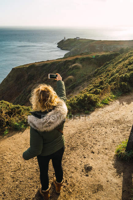 Vue arrière de la femme prenant des photos de paysage marin avec smartphone — Photo de stock