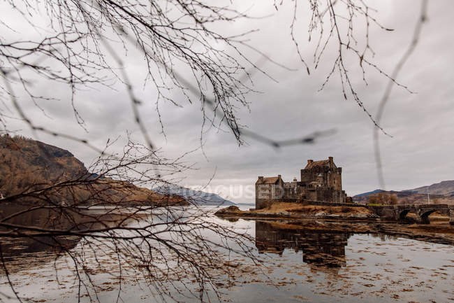 View through branches to castle at mountain lake — Stock Photo