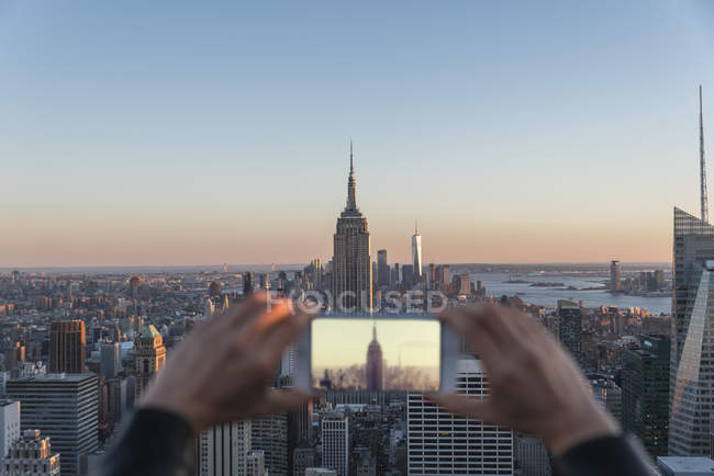 Recortar las manos femeninas tomando fotos del horizonte de Nueva York con el teléfono inteligente - foto de stock