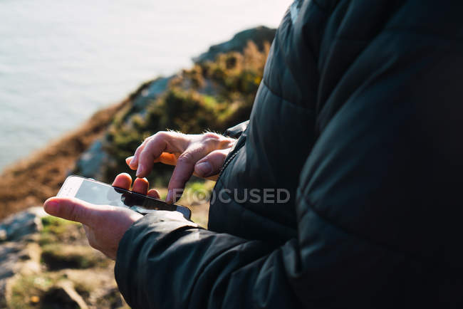 Crop man typing on smartphone at coastal hill — Stock Photo