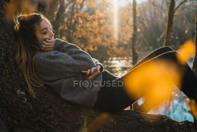 Vista lateral de la mujer soñadora acostada en el tronco en los bosques otoñales - foto de stock