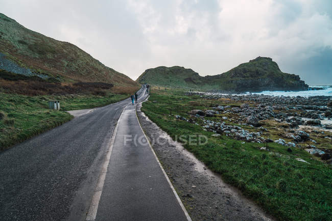 Отдаленный взгляд на туристов, идущих вместе по асфальтированной дороге на берегу моря — стоковое фото