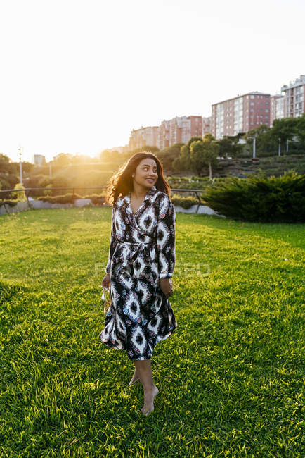 Retrato de una mujer sonriente posando sobre un césped soleado y mirando hacia otro lado - foto de stock