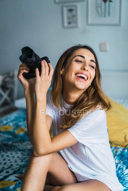 Ridendo donna seduta sul letto e tenendo la fotocamera — Foto stock
