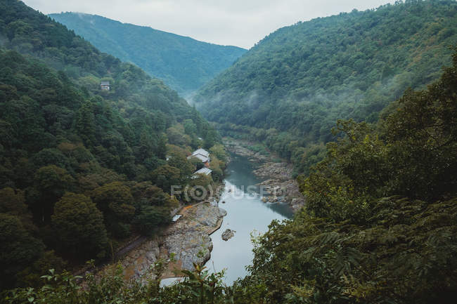 Vista para o pequeno rio correndo em desfiladeiro entre duas colinas verdes . — Fotografia de Stock