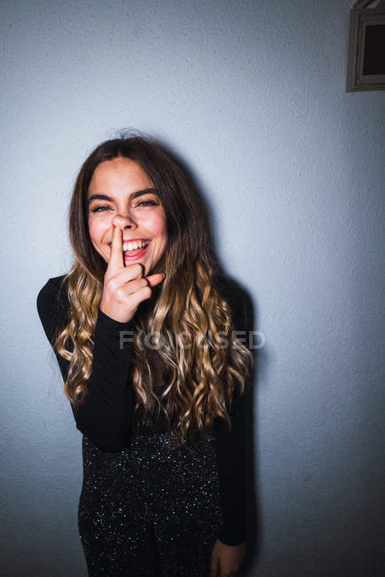 Expressive woman leaning at wall and putting finger in nose — Stock Photo