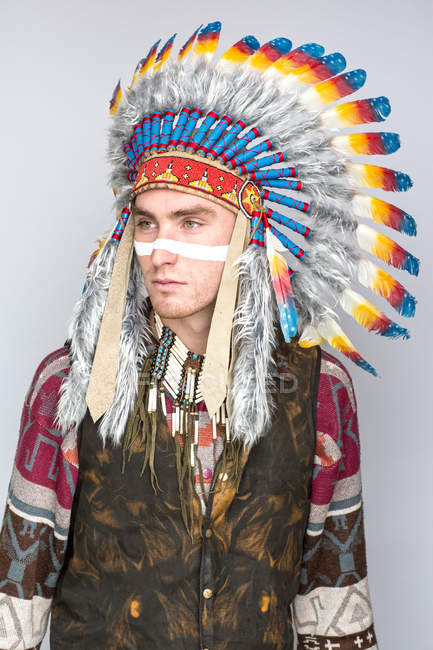 Young man with line on face posing in traditional Native American costume — Stock Photo