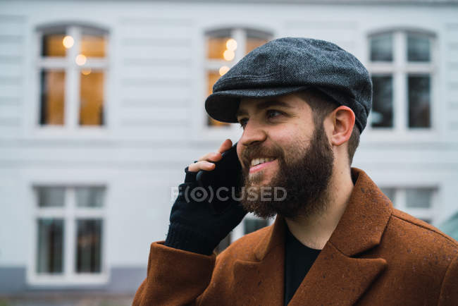 Homme barbu souriant parlant sur smartphone à la rue — Photo de stock