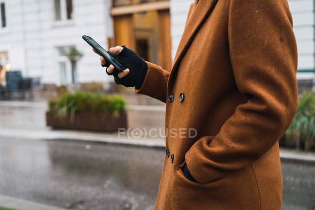 Земледелец в винтажном пальто ходит по улице и пользуется смартфоном — стоковое фото