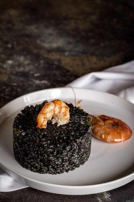 Black rice with prawns served on white plate on old table. — Stock Photo