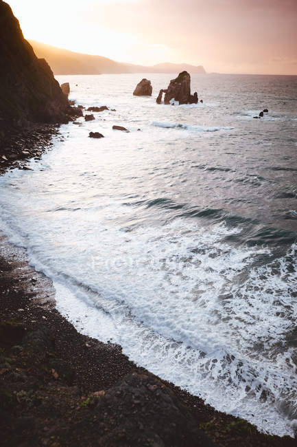 Olas tranquilas en la costa con rocas en las luces del atardecer . - foto de stock