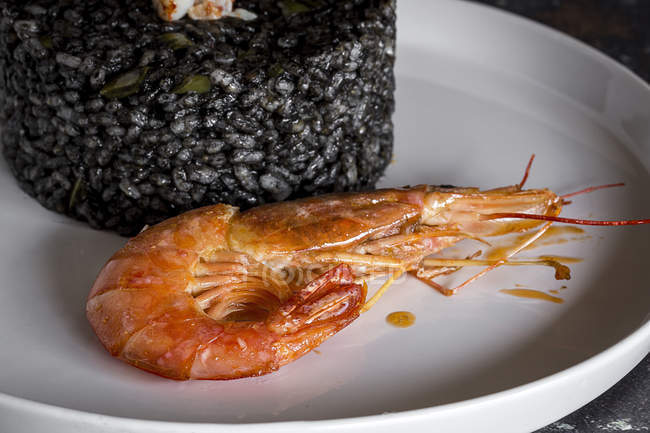 Prawn by black rice on white plate on old table. — Stock Photo