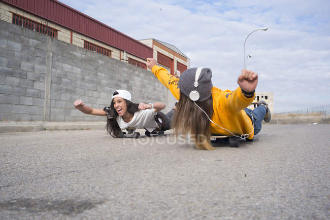 Surface level view of friends lying on longboards and riding on road — Stock Photo