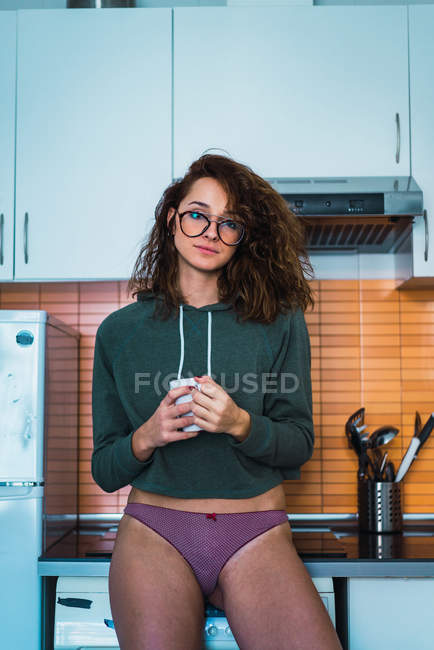 Молода жінка в трусиках стоїть з чашкою на кухні вдома . — стокове фото