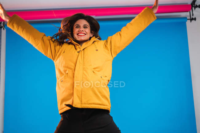 Smiling young woman posing with hands up on blue background in studio. — Stock Photo