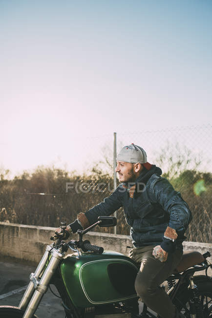 Vue latérale de l'homme assis sur la moto au coucher du soleil — Photo de stock
