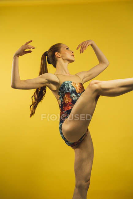Side view of ballet dancer with raised up leg on yellow background — Stock Photo