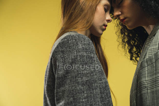 Vista laterale di coppia femminile in piedi con gli occhi chiusi e coccole su sfondo giallo . — Foto stock