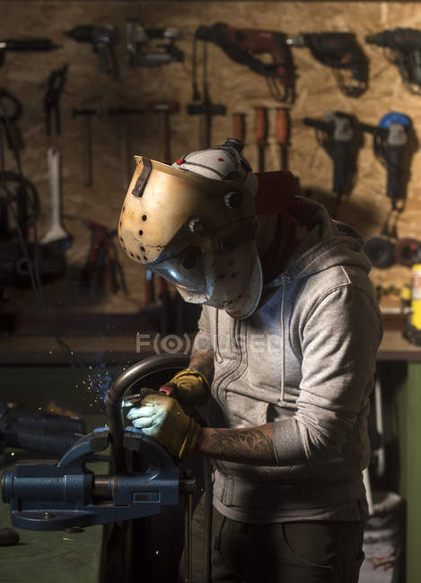 Vista lateral del mecánico en tubo de soldadura de máscara en el taller - foto de stock