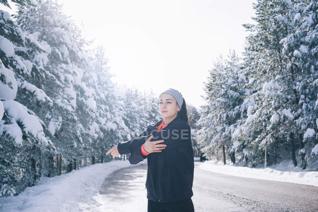 Portrait of woman doing exercise and warming muscles on snowy road. — Stock Photo