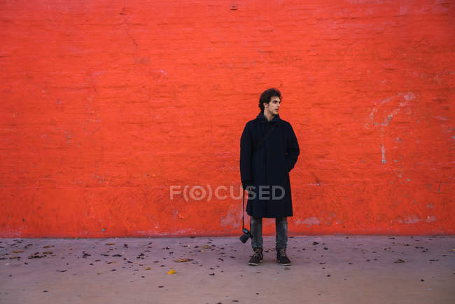 Чоловік з камерою позує на помаранчевій стіні — стокове фото