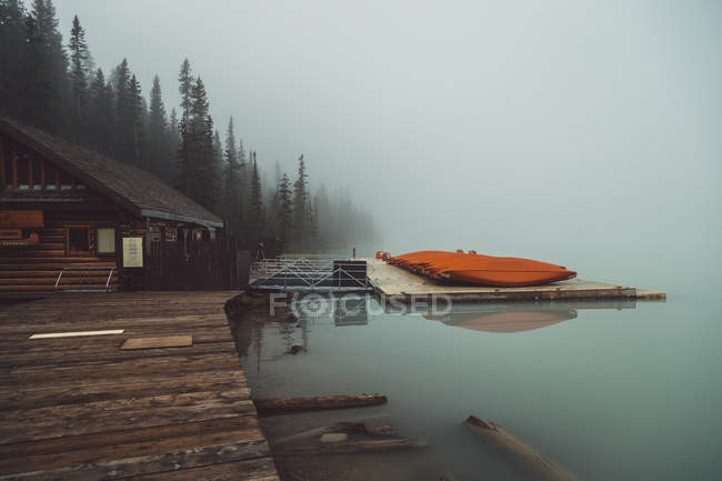 Wooden house by jetty on foggy lake — Stock Photo