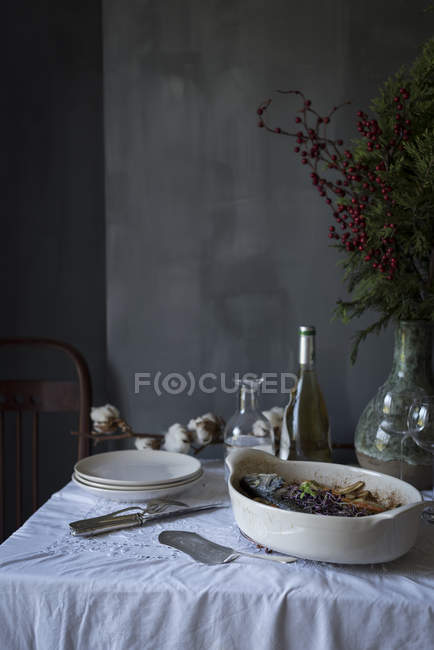 Still life of table with stack of plates and bowl with cooked fish — Stock Photo
