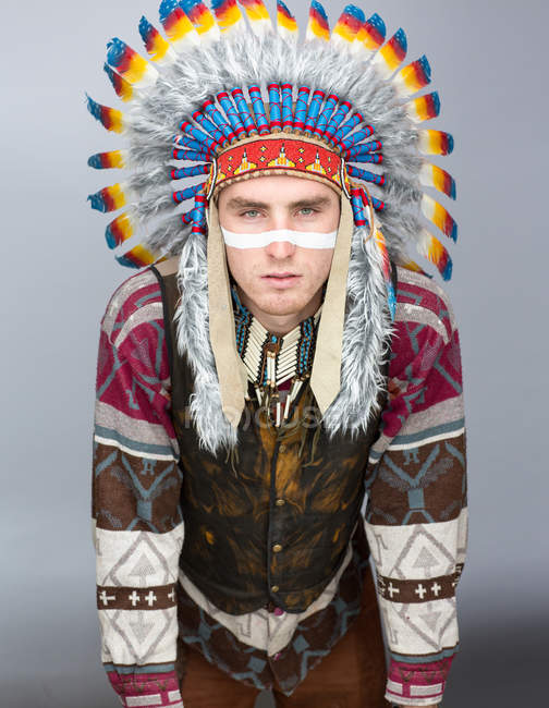 Portrait of young man with painted line on face posing in Native American costume. — Stock Photo