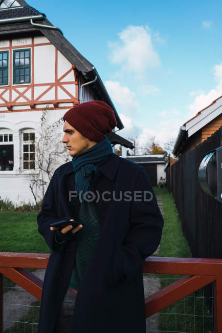 Mann lehnt mit Smartphone am Zaun und schaut weg — Stockfoto