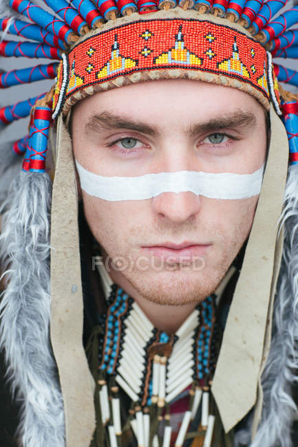 Portrait of man with painted line on face posing in traditional Native American costume and looking at camera — Stock Photo