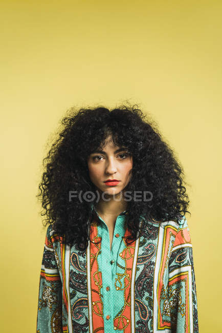 Curly mulher posando no fundo amarelo e olhando para a câmera — Fotografia de Stock
