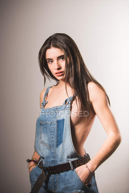 Brunette topless girl posing in denim overall at studio — Stock Photo