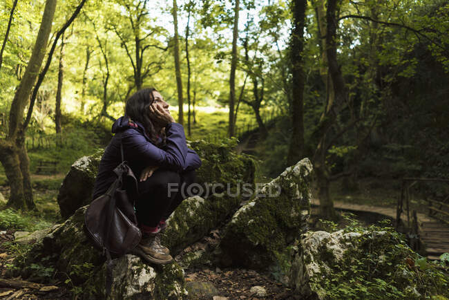 Side view of tourist woman sitting on stone in forest and resting. — Stock Photo