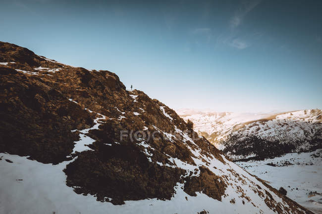 Отдаленный вид туриста, стоящего на снежном склоне горы на фоне идиллического пейзажа — стоковое фото