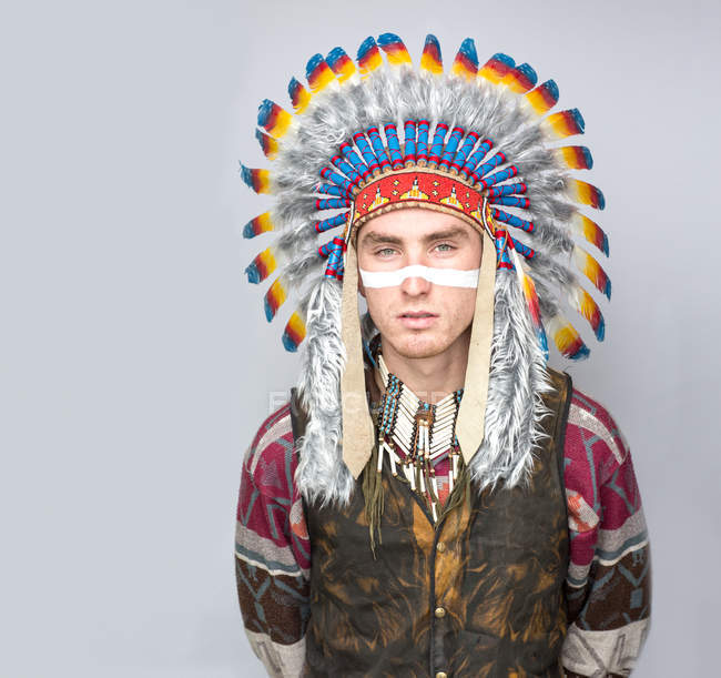Portrait of man with painted line on face posing in traditional Native American costume. — Stock Photo