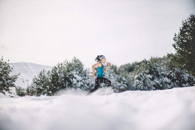 Vista lateral de la mujer deportiva corriendo en el campo cubierto de nieve . - foto de stock