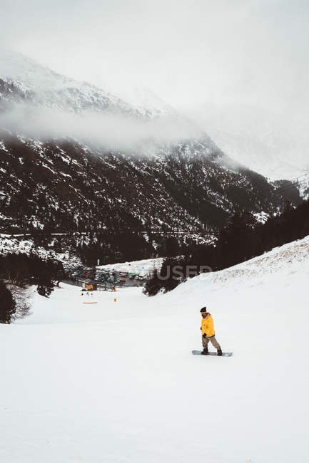 Турист в жовтій куртці катається на сноуборді на сніжному гірському схилі . — стокове фото
