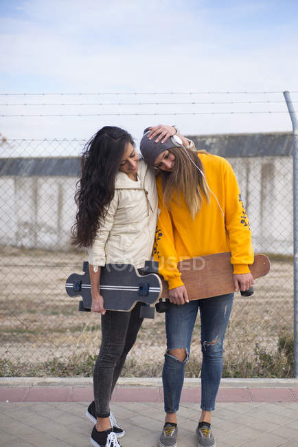 Dos chicas con longboard abrazar y divertirse en la calle - foto de stock
