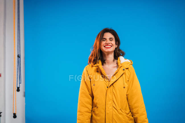 Весела жінка в жовтій куртці на синьому фоні — стокове фото