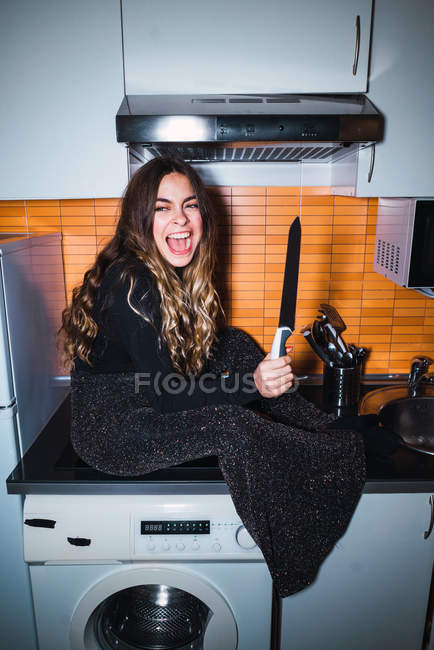 Expressive woman posing with knife at kitchen — Stock Photo