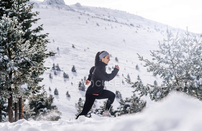 Vista lateral da mulher esportiva correndo na área nevada . — Fotografia de Stock
