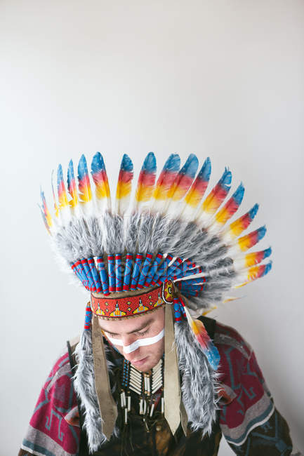 Jovem com em traje tradicional nativo americano olhando para baixo no fundo branco — Fotografia de Stock