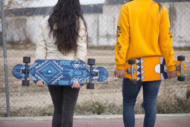 Visão traseira de duas meninas posando com longboard na cena de rua — Fotografia de Stock