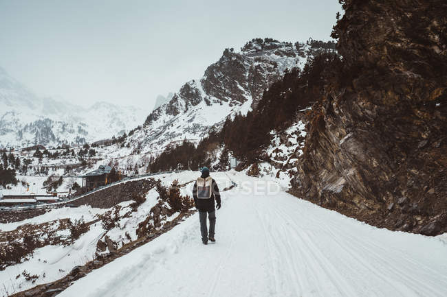 Rear view of backpacker walking on snowy mountain road — Stock Photo