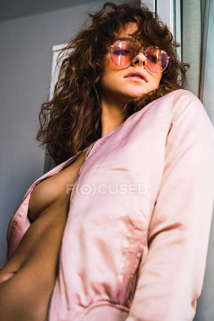 Молодая женщина в куртке на обнаженном теле и розовых солнцезащитных очках — стоковое фото